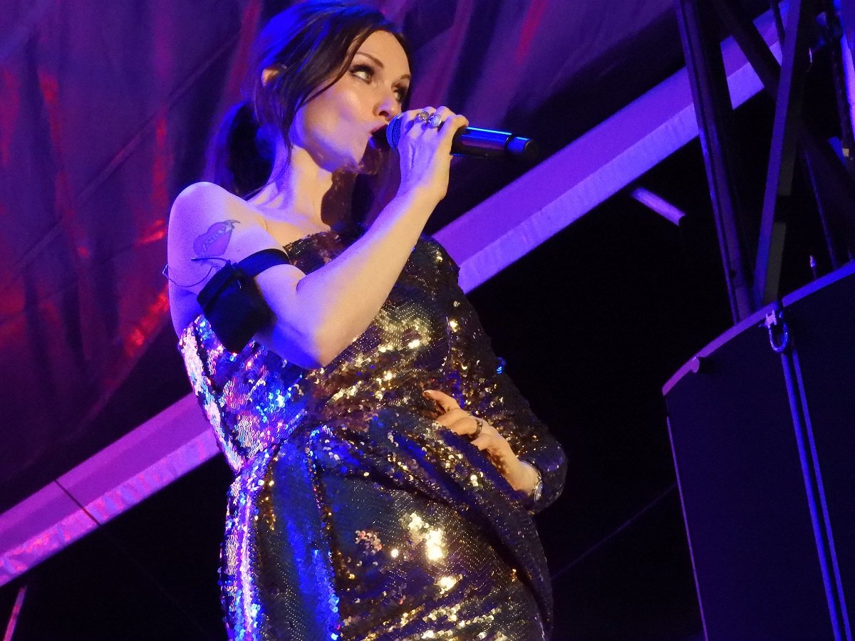 A woman singing, wearing a glittery dress. Purple lighting around her.