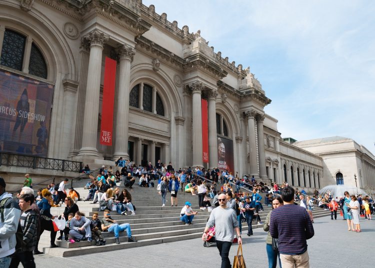 Crowds gathered on the steps of a grand neoclassical museum with tall columns and red banners.