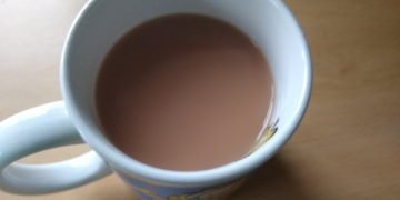 Top-down view of a blue mug filled with light brown tea or coffee on a wooden table, handle to the left.