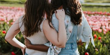 Two women stand next to each other with an arm around the other, looking at a field of tulips