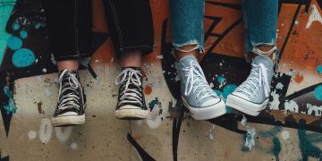 Four legs with jeans and sneakers on the feet, danging down from a wall with graffiti on it. The rest of the individuals is not visible in the picture