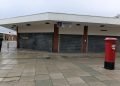 Breck Road Library, large one-storey corner building with all windows shuttered up, a red postbox in front and a single person walking by.