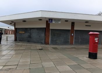 Breck Road Library, large one-storey corner building with all windows shuttered up, a red postbox in front and a single person walking by.